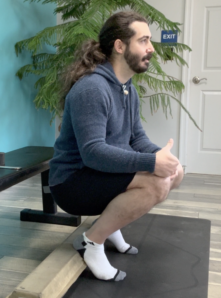 John demonstrating knees over toes knee mobility in a heel elevated squat